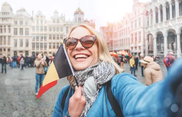 Deurstickers Vrouwelijke toerist staat met de vlag van België op de achtergrond van de Grote Markt of het Grote Marktplein in Brussel © LALSSTOCK