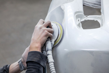 Preparation for painting a car element using sander and putty by a service technician leveling out...