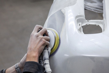 Preparation for painting a car element using sander and putty by a service technician leveling out...