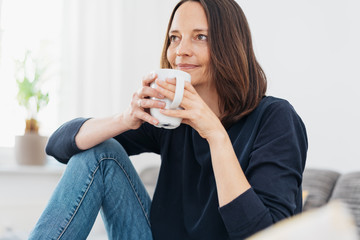 lächelnde Frau sitzt auf dem Sofa und trinkt entspannt eine Tasse Kaffee