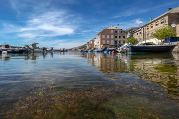 Reflection of houses in blue sea in little fishing port in town Karlobag in Croatia with Velebit mountain in background