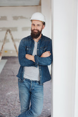 Architekt mit weißem Helm lehnt an einer Wand auf der Baustelle