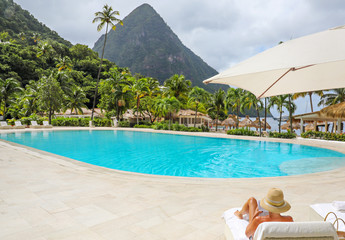 Woman sitting by a swimming pool reading a book in the Caribbean.
