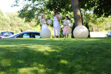 Dziewczynki z balonami na wzniesieniu pokrytym zieloną trawą. - obrazy, fototapety, plakaty