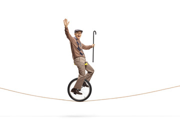 Elderly man riding a unicycle on a rope and holding a walking cane © Ljupco Smokovski