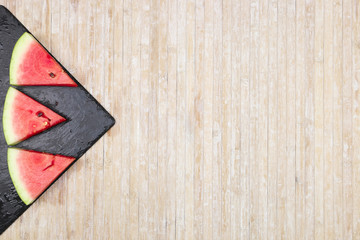 Triangular slices of watermelon on a black slate plate forming geometric games for copy space on a light wooden background