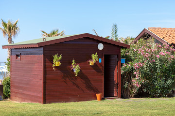 Little brown painted shed in the middle of a garden with green grasses and trees