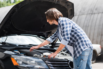 calm man standing near broken auto and looking at open trunk, car insurance concept