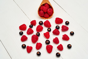 Ripe sweet raspberries and black currant in ice cream waffle cone, copy space. Fresh berries on white wood background. Summer and healthy food concept