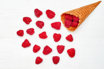 Ripe sweet raspberries in ice cream waffle cone, copy space. Fresh berries on white wood background, free space. Summer and healthy food concept