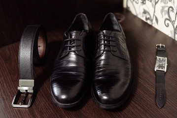 Close up of black male shoes, belt and watches on wood table background, copy space. Modern man accessories. Wedding details. Male casual outfits
