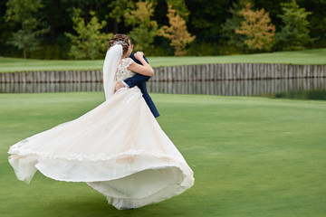 Full length body portrait of young bride and groom dancing on golf course, back view. Happy wedding...