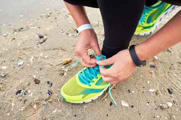 Woman tying running shoe laces preparing for run on ocean beach, copy space, closeup. Female fitness runner getting ready for jogging outdoors