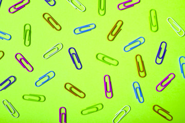 Colorful paper clips on lime green background, copy space. Top view, flat lay. Back to school, business concept. Abstract background