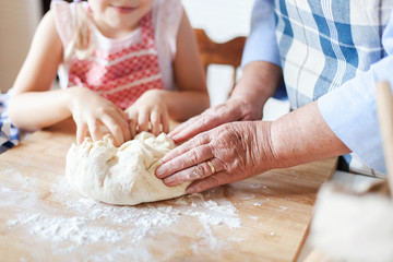 Family is preparing dough for baking in kitchen. Graceful hands of retired woman and kid are cooking homemade pastries or pizza.