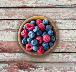 Top view. Blue and red berries in bowl. Ripe raspberries and blueberries on a wooden background. . Background of mix berries with copy space for text. Mix berries on rustic background. 