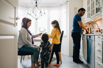 Naklejka premium Woman sitting with children while man washing utensils in kitchen at home