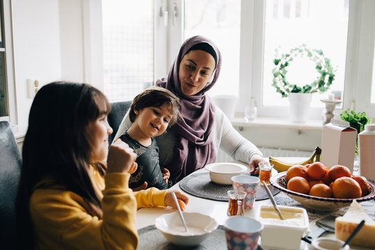 Smiling mother talking to children while having breakfast at dining table