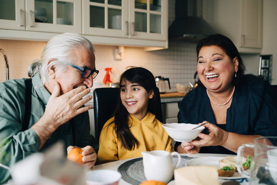 Elderly man talking to grandchild and woman with milk mustache during breakfast at home
