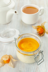 Dessert in a jar with a cup of black tea, served on a total-white background: creamy tiramisu iwth whipped mascarpone, savoyardi and mango sauce