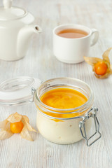 Dessert in a jar with a cup of black tea, served on a total-white background: creamy tiramisu iwth whipped mascarpone, savoyardi and mango sauce