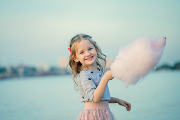 Portrait of a little girl who is resting in nature and eating cotton candy depicting pleasure and...