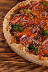 Top view of european thin-dough pizza with chicken fillet, ham, mozzarella cheese, tomatoes and pepperoni on a wooden background