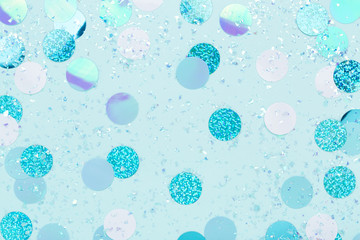 Carnival decorations of iridescent confetti and sparkles on pastel blue background. Trendy holiday backdrop. Flat lay.