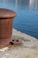 Large rusty bollard on the edge of the river or sea. Close-up photo Water reflections