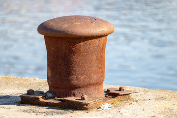 Naklejka premium Large rusty bollard on the edge of the river or sea. Close-up photo Water reflections