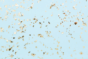 Golden foil confetti on light blue background. Festive, party or holiday glowing backdrop. Flat...