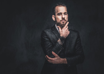Portrait of a stylish serious bearded male, wearing an elegant suit on a dark background.