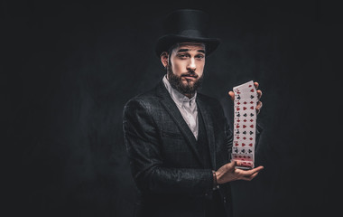 Magician showing trick with playing cards on a dark background.