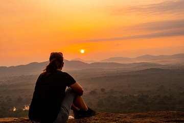 Girl sitting on Pidurangala Rock enjoying sunrise view over Sigiriya rock