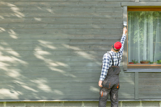Man worker painting wooden house exterior wall with paintbrush and wood protective color