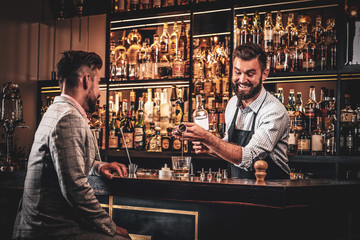 Handsome modern man in checkered suit is consuming alcohol at trendy bar.