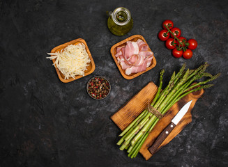 Preparing bacon wrapped asparagus on dark table.  Сooking asparagus. Ingredients for cooking on black background.
