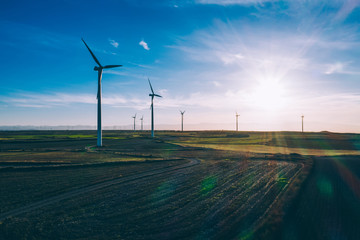 Aerial scenic view of renewable windmills turbines supplying cultivation area with eco power getting energy from wind blowing on vast area of agriculture meadows next to sea. Alternative electricity