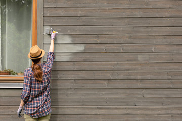 Woman worker painting wooden house exterior wall with paintbrush and wood protective color