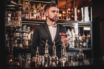 Elegant handsome man in classic suit is consuming alcohol at the nice bar.
