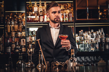 Elegant handsome man in classic suit is consuming alcohol at the nice bar.