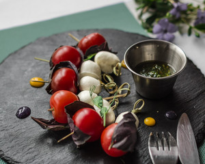 Cherry tomatoes with mozzarella cheese on skewers, on a black background. Italian snack. Restaurant menu.