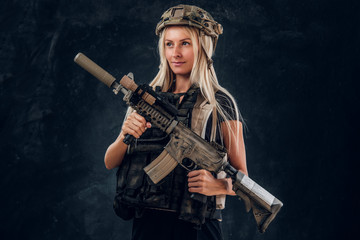 Fototapeta na wymiar Beautiful fragile blond girl with machine gun in full army uniform and helmet.
