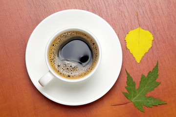 White cup with black coffee and autumn leaves
