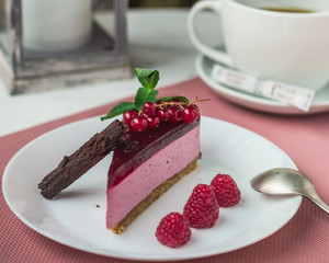 Berry cheesecake with fresh raspberries and chocolate stick on a plate. Dessert and a cup of tea on a white table.