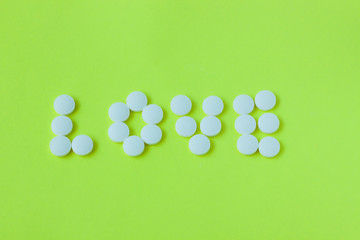 Pills in a shape of a word Love on a yellow background. Flat lay, top view, minimalistic style.