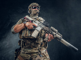 Military man in full equipment with wach on his hand is holding machine gun while posing for photographer over dark background. © Fxquadro