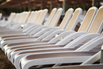 Row of clean white plastic deck chairs on a sandy beach close up