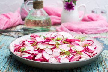 Fresh salad of pieces of radish and dill on a plate on a wooden table. Ready snack for a diet