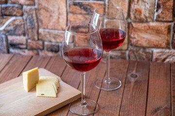two glasses of red wine and sliced cheese on a wooden table